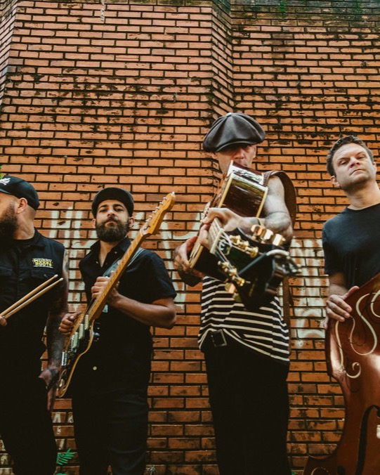 A banda com instrumentos diante de um muro de tijolos